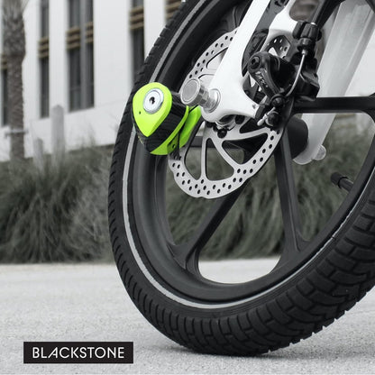 In this image, we see a modern and vibrant lime green disc lock attached to the front brake disc of a motorcycle. The color of the lock provides a striking contrast against the grayscale background, drawing the viewer’s attention immediately to the security device. The disc lock is compact, yet its placement suggests a robust and effective deterrent against theft. The "BLACKSTONE" branding is discreetly positioned in the lower right corner, suggesting a focus on the product's sleek design and functionality