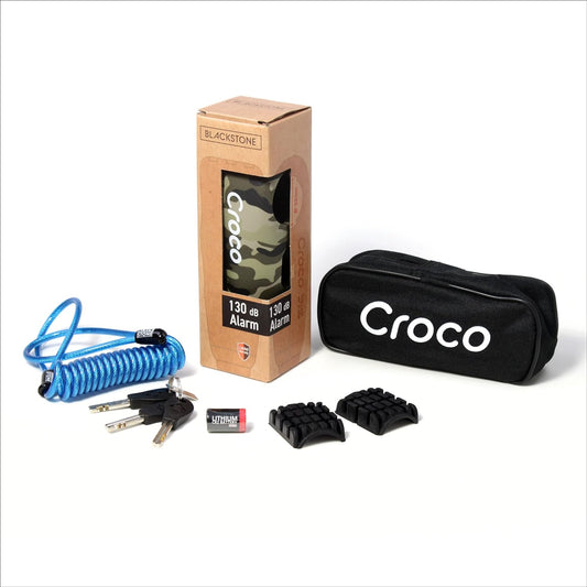 The image shows a product set which includes a Blackstone Croco alarm lock in its packaging, a Blue coiled cable, a black carrying pouch with the text "Croco" on it, three keys, a battery, and Two rubber pads for the lock, offering customization for various handlebar thicknesses or preferences. The items are neatly displayed, presumably for marketing or sales purposes