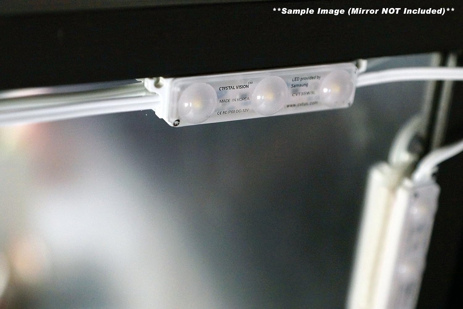 The image shows a close-up of Crystal Vision's LED module, provided by SAMSUNG and made in Korea. The module is attached to the underside of a surface, possibly a mirror frame, indicating it's designed for discreet installation. A note clarifies that this is a sample image and the mirror is not included. The focus is on the LED module's design and branding details.