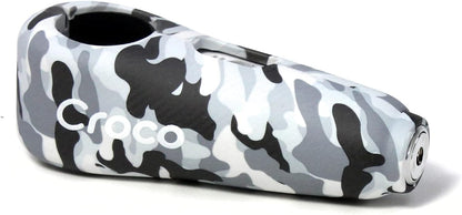 The image shows a close-up view of a Camo white Croco lock with a carbon fiber-like texture on its surface. The lock appears robust and is branded with the Croco logo in white letters, suggesting a focus on strong visual branding. The keyhole is at one end of the lock, hinting at a high-security cylinder mechanism. The design is sleek and modern, and the overall impression is that of a sturdy, reliable lock for securing valuable items